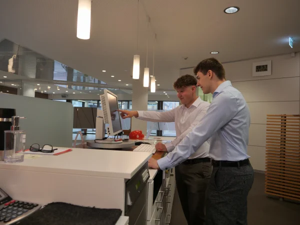 An einem Beratungsplatz in der Kreissparkasse stehen zwei junge Mitarbeitende gemeinsam an einem Bildschirm.